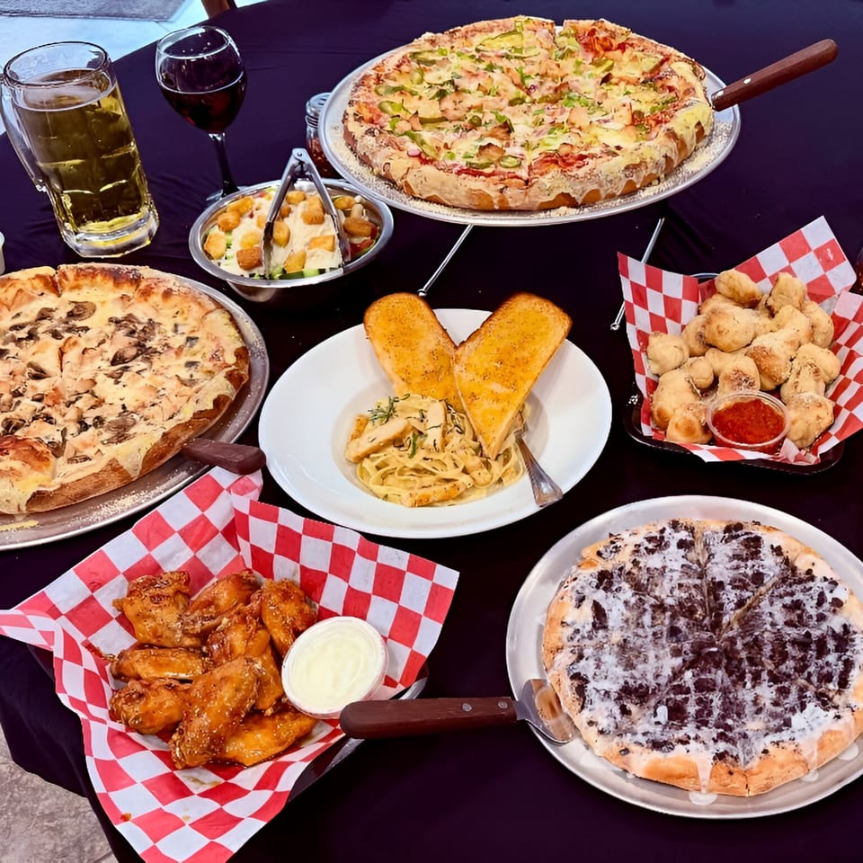 A table laden with 2 Brother's Pizza dishes, including various pizzas, pasta, wings, and drinks.