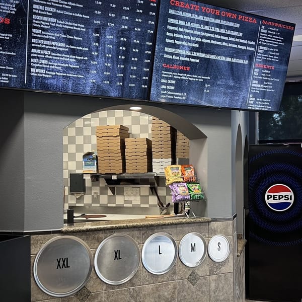 A pizza counter with menus, stacks of pizza boxes, and pizza pans of various sizes.