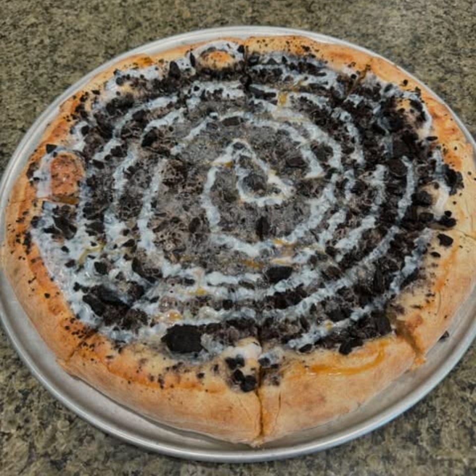 A dessert pizza from 2 Brother's Pizza, topped with crushed cookies and white icing in a spiral.