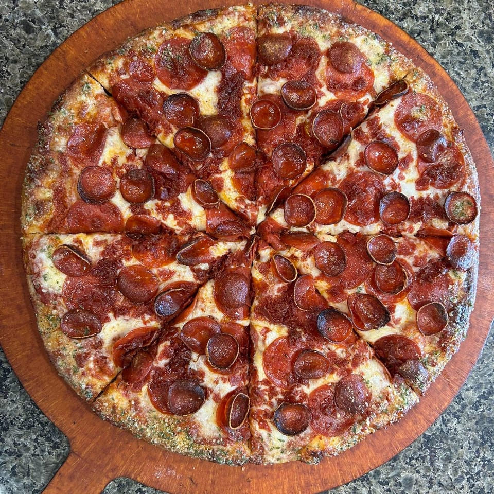 A whole pepperoni pizza from 2 Brother's Pizza, sliced into eight pieces on a wooden peel.