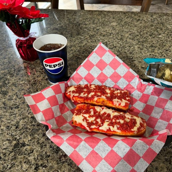 Two cheesy breadsticks with red sauce, a Pepsi, and a red poinsettia on a granite table.