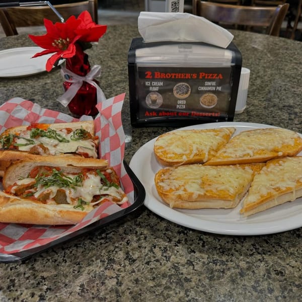 Meatball subs and cheesy garlic bread on a granite table with a 2 Brother's Pizza dessert menu.