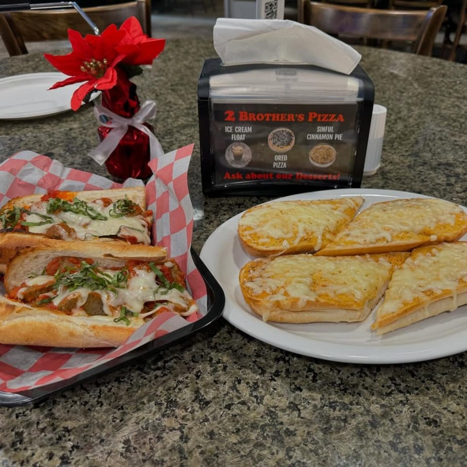 Meatball subs and cheesy garlic bread on a granite table with a 2 Brother's Pizza dessert menu.